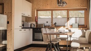 A modern kitchen with wooden walls, a dining area with a table and chairs, and a large window. - Your Bright Chalet With Sauna in Bichlbach (Bichlbach)