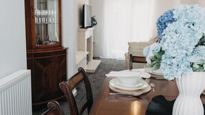 Une salle à manger avec une table en bois dressée pour quatre personnes, un buffet aux portes vitrées et un vase rempli de fleurs.