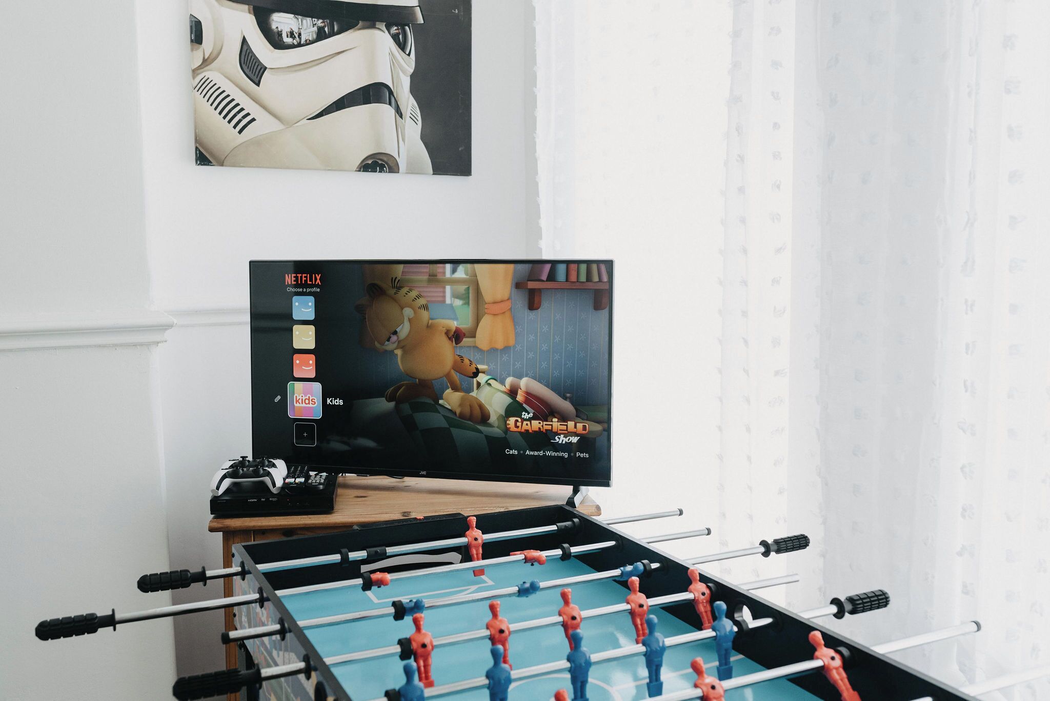 A foosball table, a television displaying 'The Garfield Show', and a poster of a white robot on the wall.