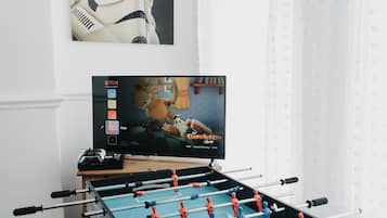 A foosball table, a television displaying 'The Garfield Show', and a poster of a white robot on the wall.