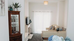 Un salon avec un meuble en bois, un canapé, un téléviseur et une fenêtre avec des rideaux.