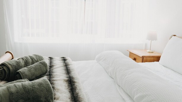 Une chambre à coucher avec un lit, une table de chevet avec une lampe et une fenêtre avec des rideaux légers.