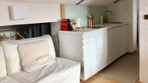 En kompakt opholdsstue med tekøkken, sofa og et lille spisebord.
