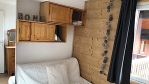 Et værelse med en hvid sofa, træskabe, et vindue med gardin og en vægmonteret lampe.