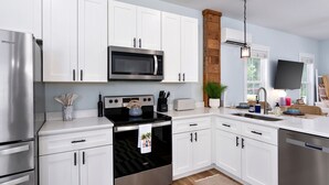 Una cocina moderna con gabinetes blancos, electrodomésticos de acero inoxidable, microondas, estufa y lavavajillas.