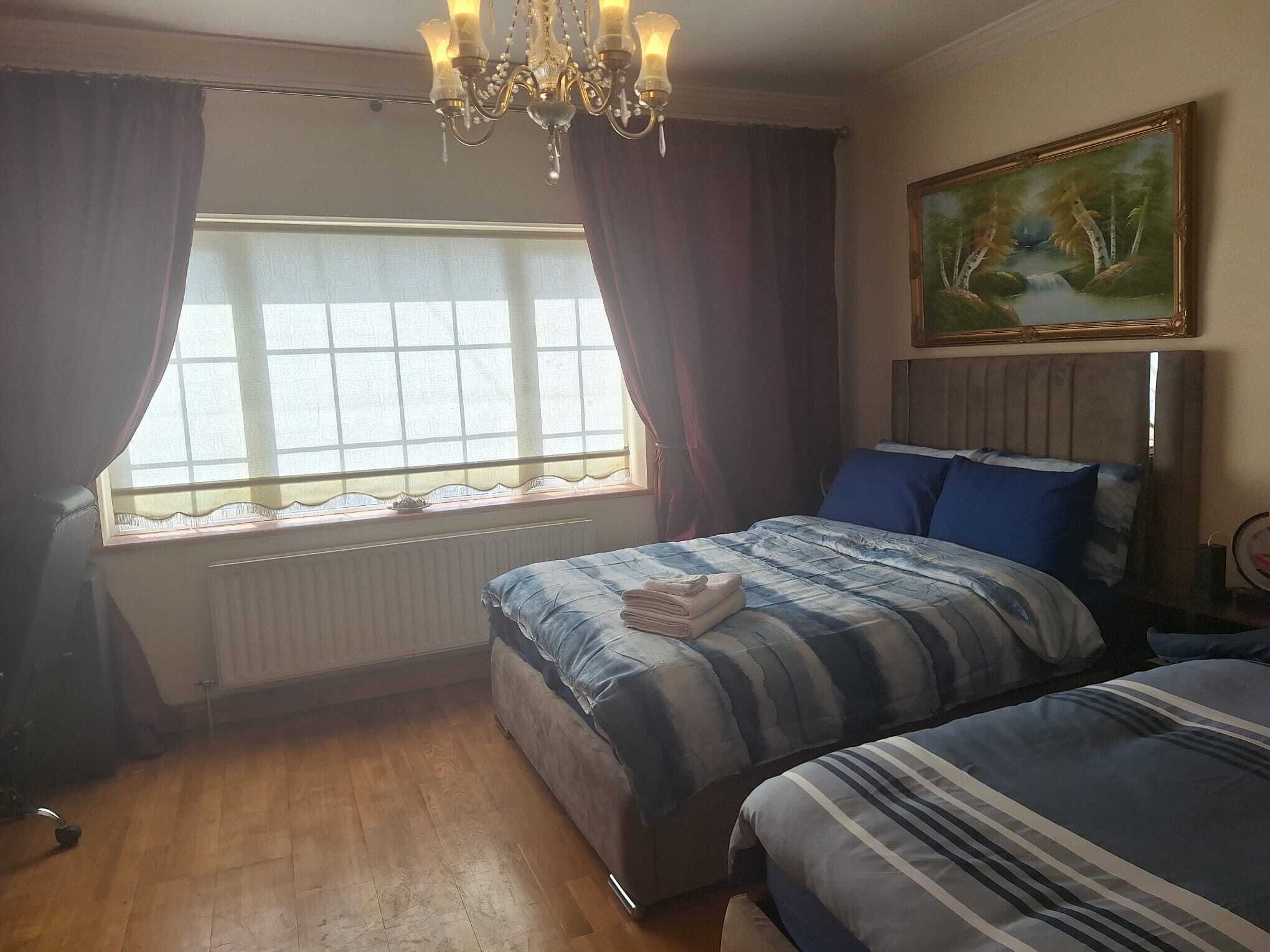 Une chambre avec deux lits, une fenêtre avec des rideaux, un radiateur, un tableau au mur et un lustre.