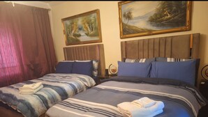 A hotel room with two beds, a wooden headboard, a painting, and a nightstand with a lamp.