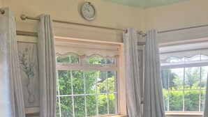A living room with a grey sectional sofa, a red leather chair, a clock on the wall, and a window with curtains.