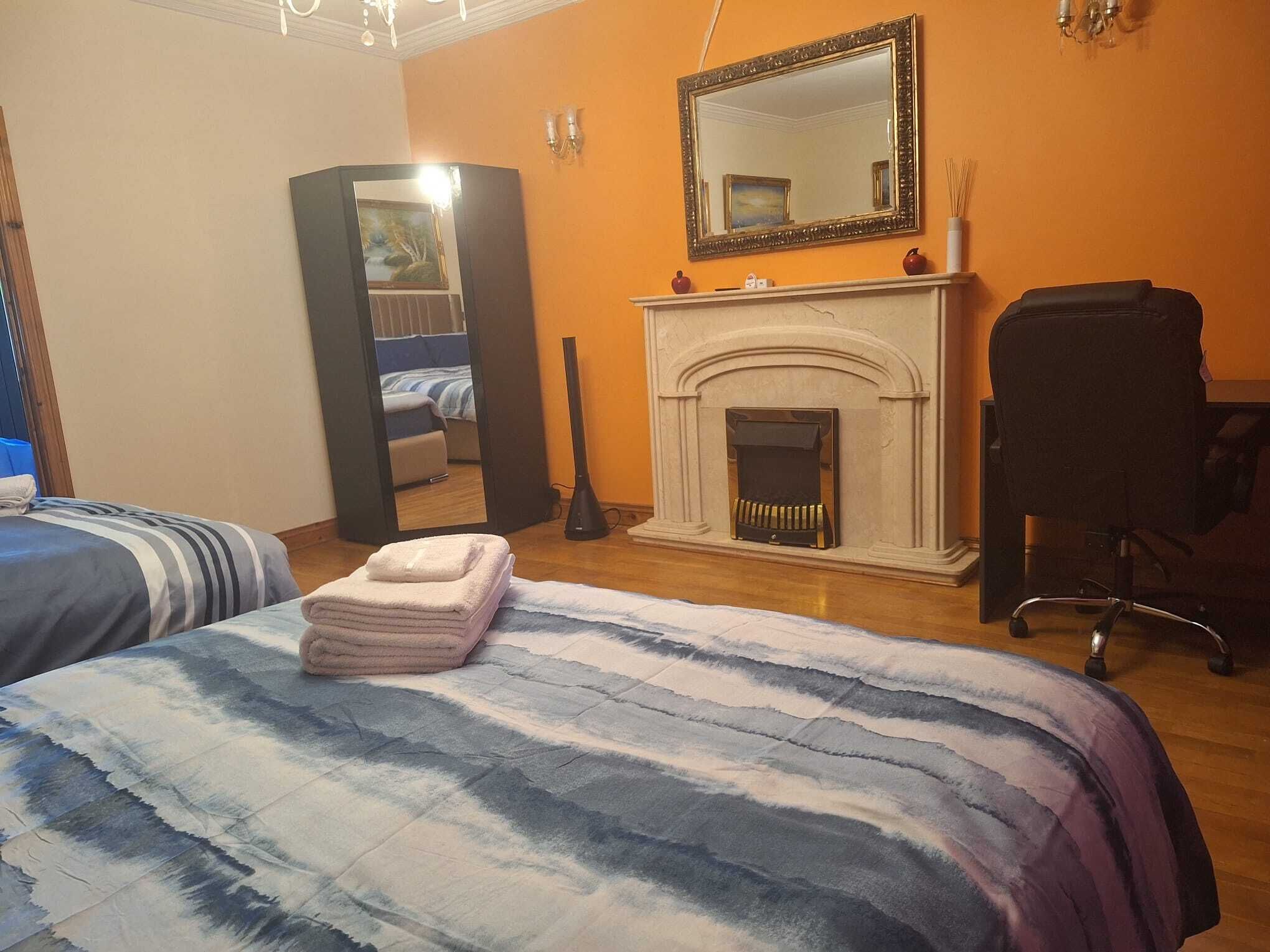 A bedroom with two beds, a fireplace, a mirror, and a chair.