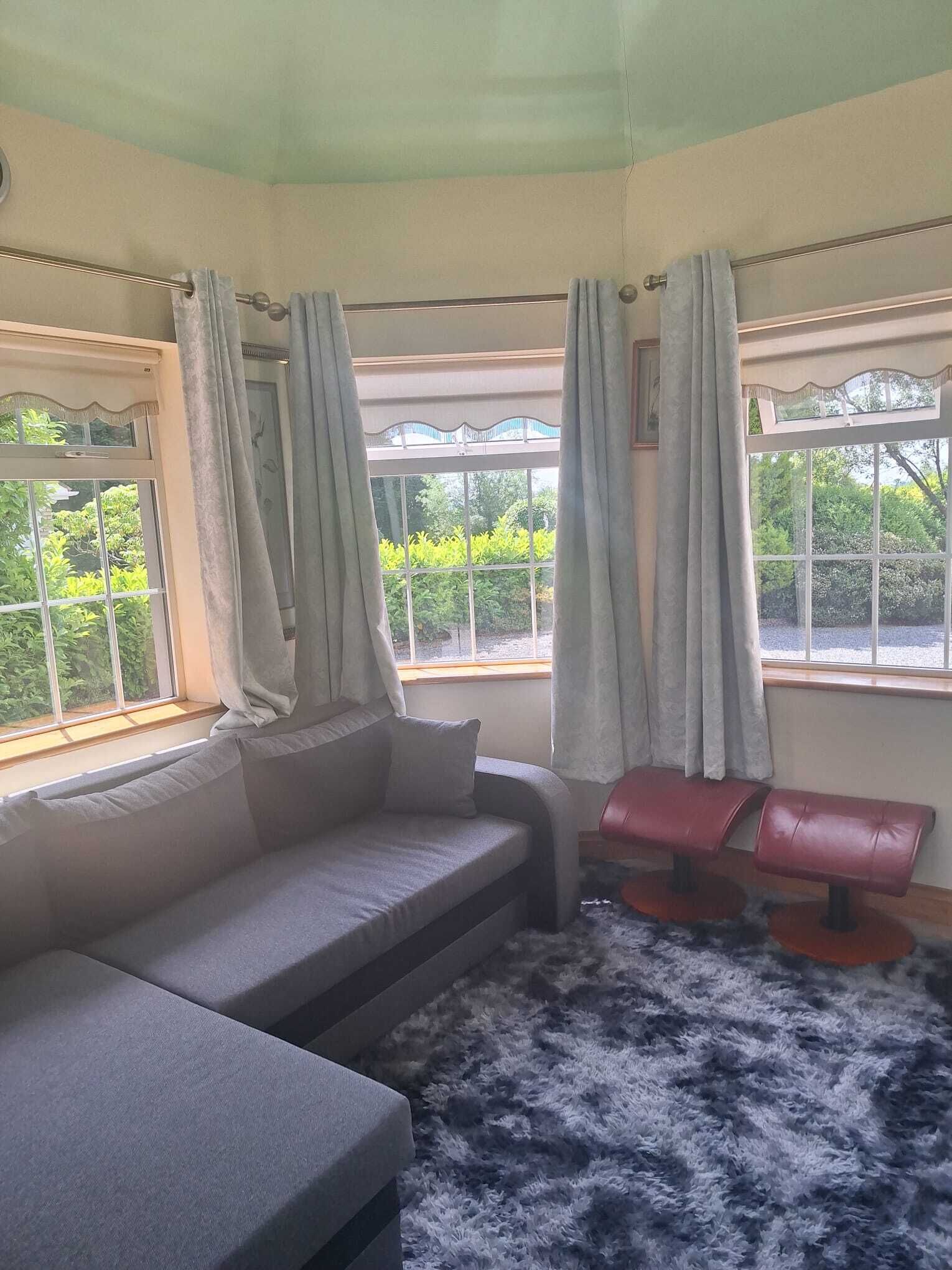 A room with a sofa, two red chairs, a fluffy rug, and large windows with curtains.