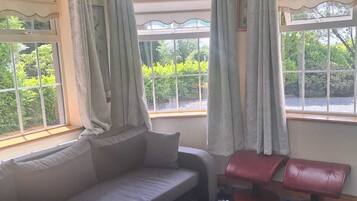 A room with a sofa, two red chairs, a fluffy rug, and large windows with curtains.