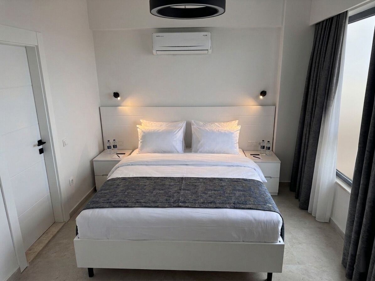 Une chambre d’hôtel moderne équipée d’un lit, de tables de chevet, d’un appareil de climatisation et d’une fenêtre avec des rideaux.