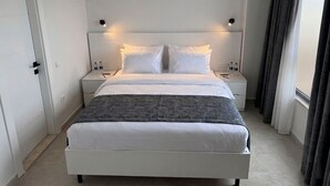 Ett modernt hotellrum med en säng, sängbord, en luftkonditioneringsanläggning och ett fönster med gardiner.