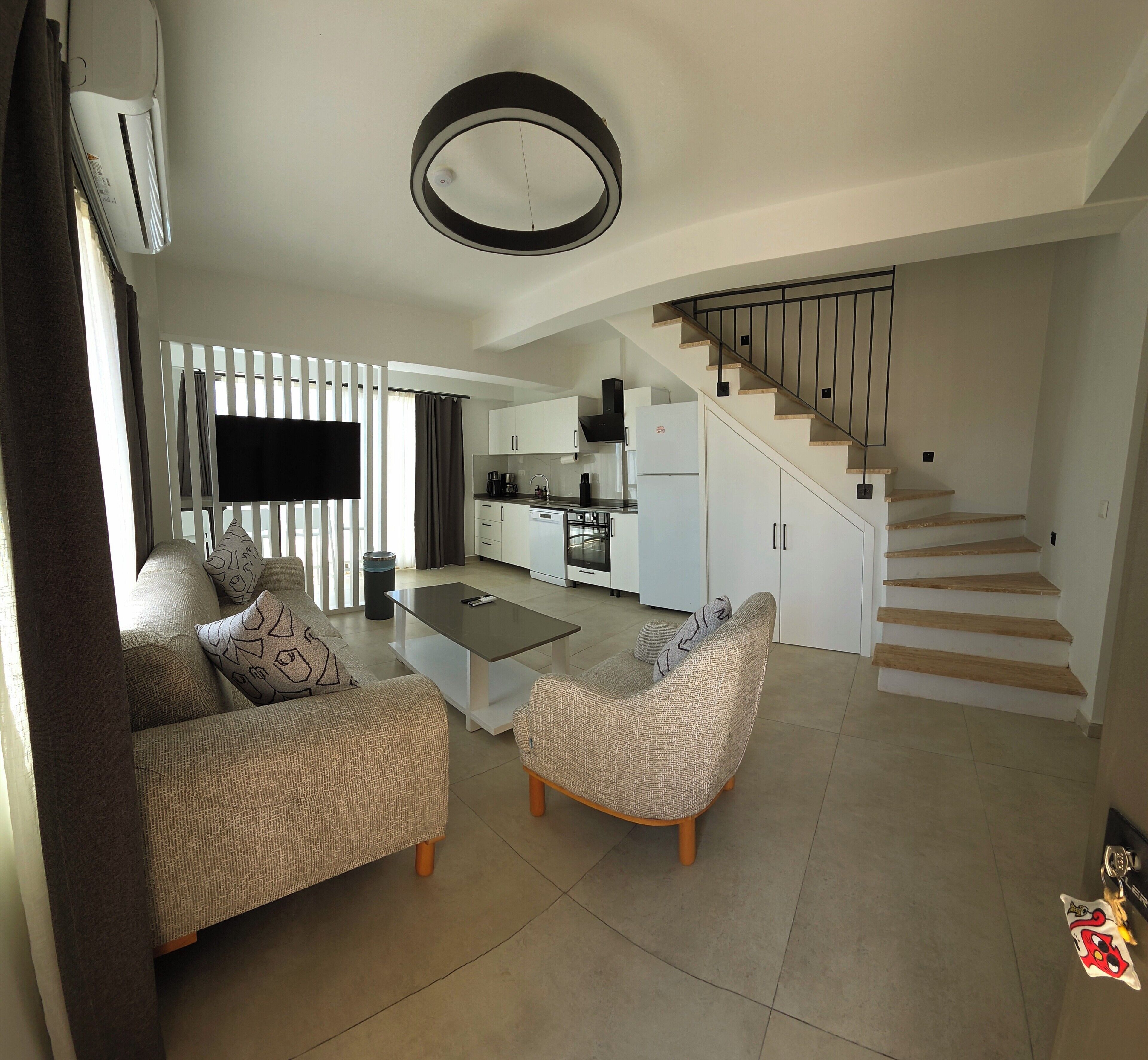 A modern living room with a sofa, coffee table, and a staircase leading to a kitchen area.