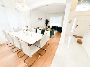 A modern dining area with a white table and chairs, a chandelier, and a view into a living room with a green sofa. - Spacious 7-bedroom condo in terrific Kissimmee with AC (Kissimmee)