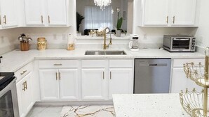 Een moderne keuken met witte kasten, een roestvrijstalen vaatwasser, een koffiezetapparaat en een broodrooster.