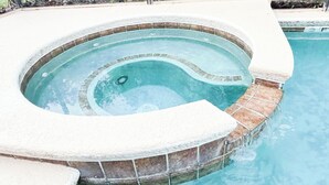 Een rond hottub met een stenen rand, omgeven door een zwembad.