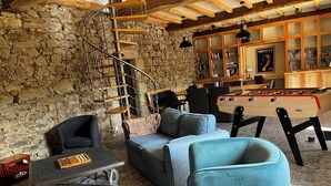 Ein gemütliches Wohnzimmer mit Steinwand, einer Wendeltreppe, einem Kicker und einer Couch.
