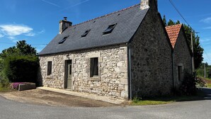 Ein Haus aus Stein mit einem geneigten Dach, zwei Fenstern und einem Schornstein.