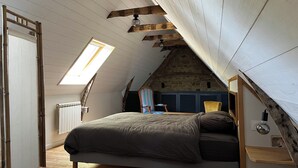 Ein Schlafzimmer im Loft-Stil mit schrägverdeckter Decke, einem Bett, einem Sessel und einem Schreibtisch.