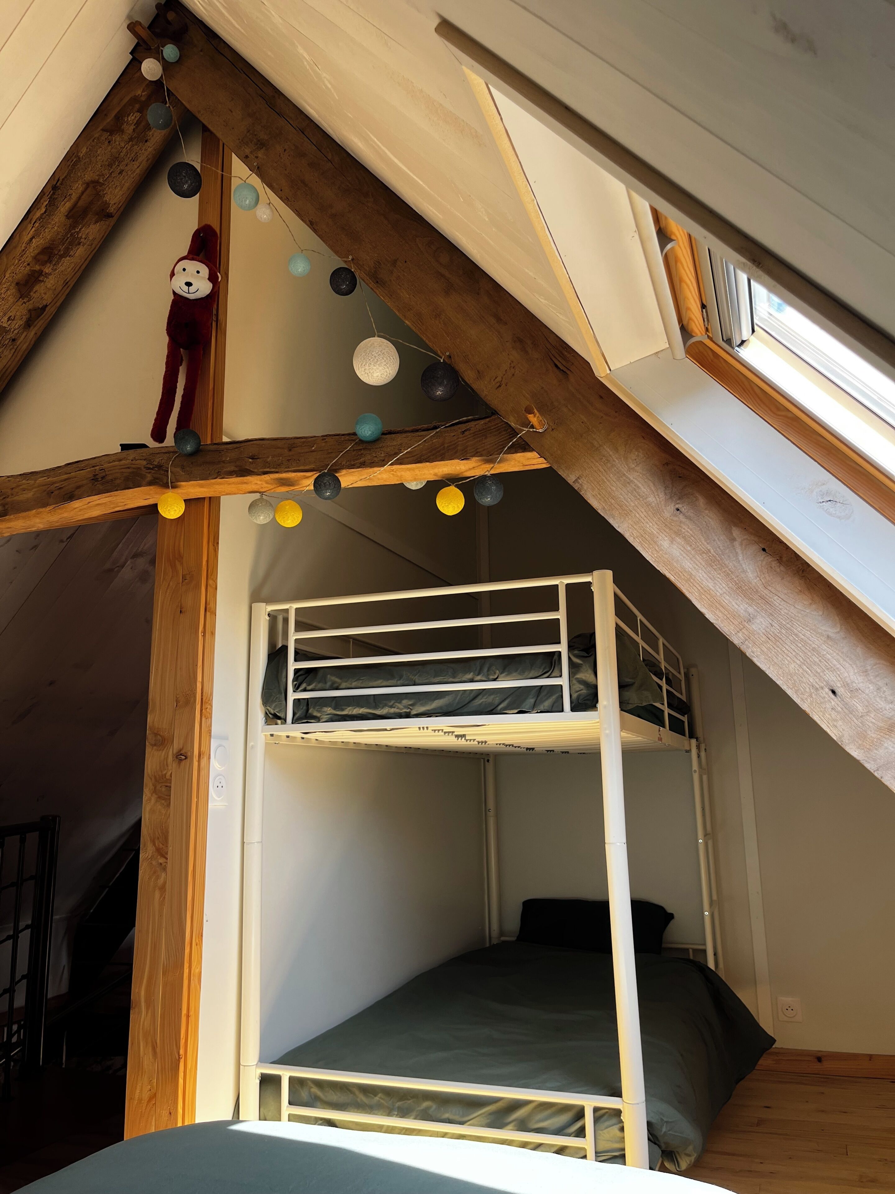 Un dormitorio estilo loft con una cama nido, vigas de madera y luces colgantes.
