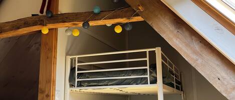 Un dormitorio estilo loft con una cama nido, vigas de madera y luces colgantes.