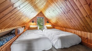 A cozy attic bedroom with two beds, wooden walls, and a window.