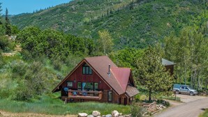 A wooden cabin with a sloped roof, a deck, and a vehicle parked nearby.