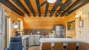 A modern kitchen with a central island, bar stools, and a blue chair.