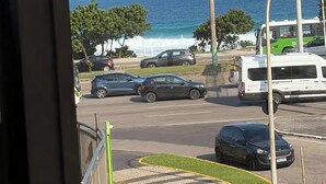 Blick auf eine Straße mit Autos, einer Palme und einem Gewässer im Hintergrund.