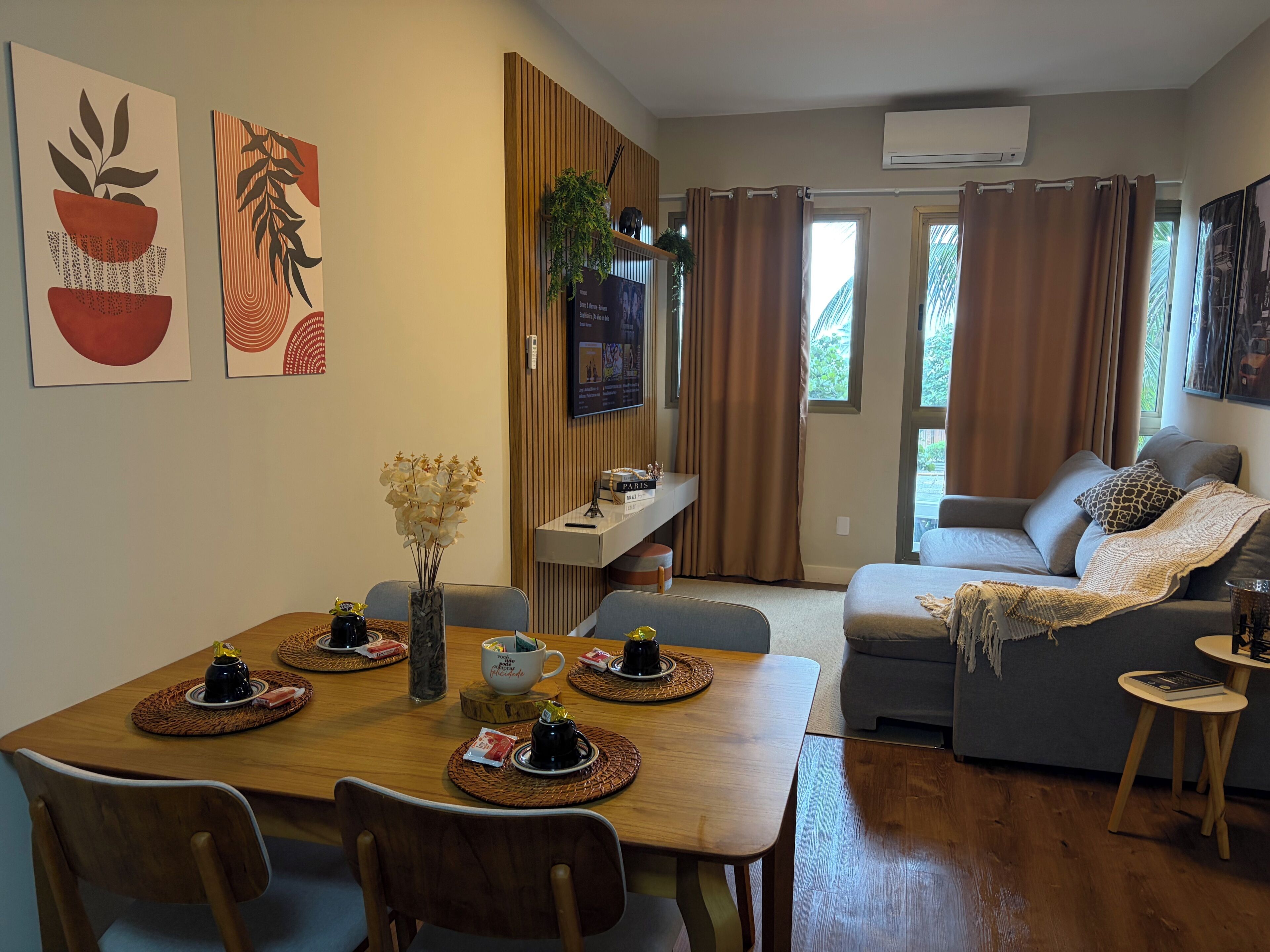 Una sala de estar con sofá, una mesa de comedor con sillas, televisor y ventana con cortinas.