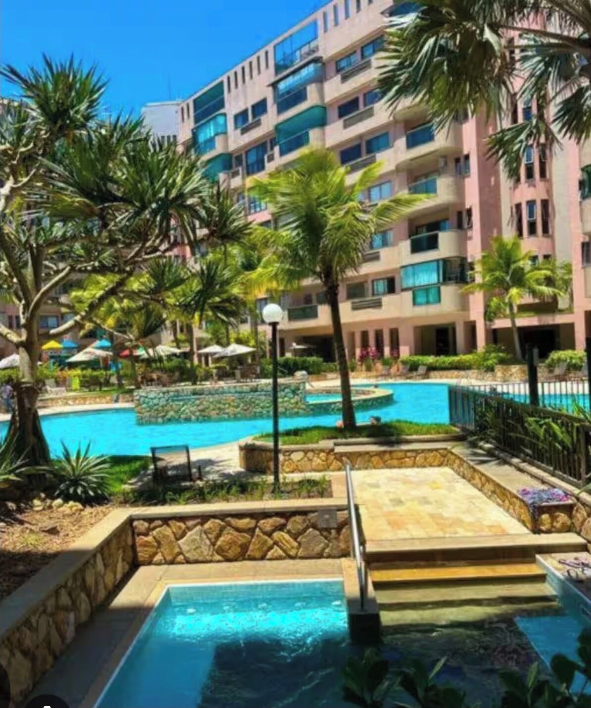 A hotel with a swimming pool, palm trees, and a multi-story building.