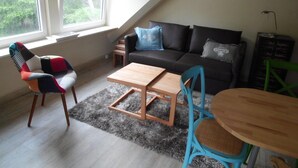 En stue i loftstil med højt til loftet, en sofa, et sofabord, en lænestol og et lille bord.