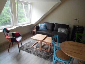 Ein Loft-Wohnzimmer mit hoher Decke, einer Couch, einem Couchtisch, einem Sessel und einem kleinen Tisch.