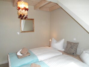 A bedroom with two beds, a mirror, and a hanging light fixture. - Ferienwohnung in Uckeritz am Strand (Ueckeritz)