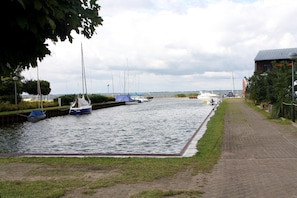 A canal with boats docked, a paved walkway, and a building with a sloped roof. - Ferienwohnung in Uckeritz am Strand (Ueckeritz)