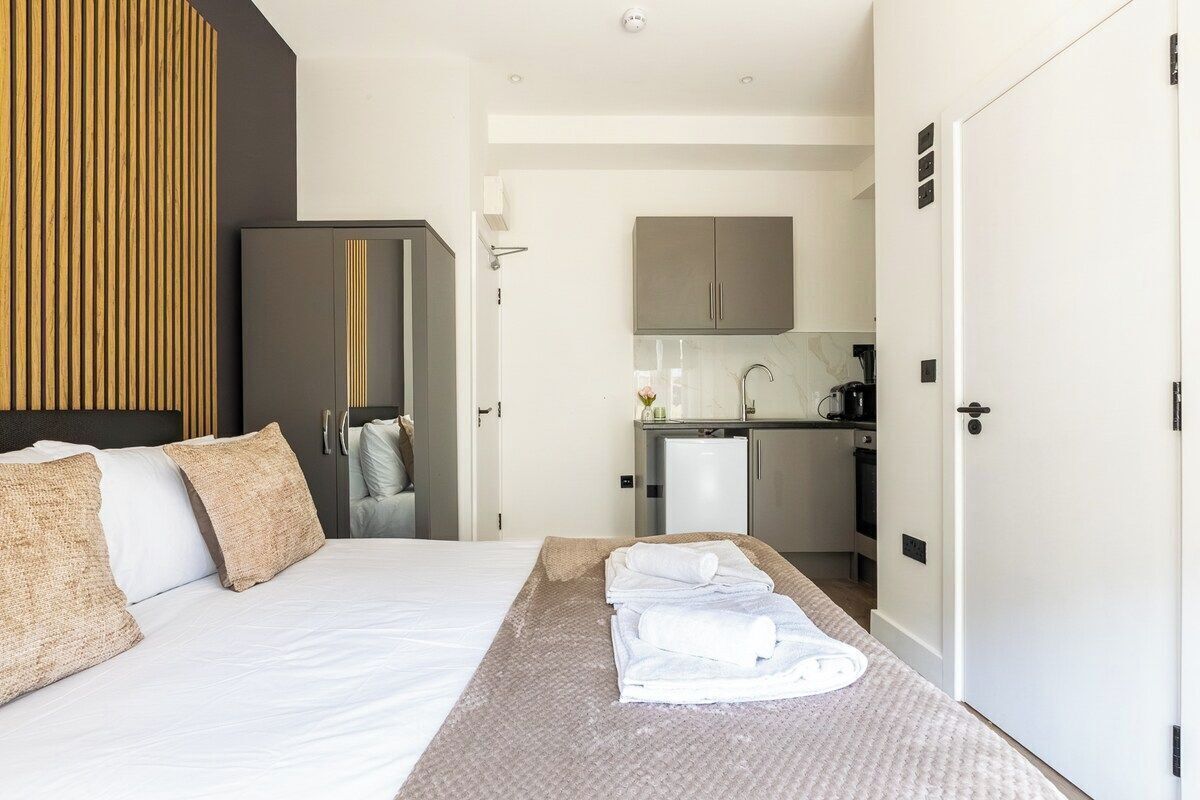A hotel room with a bed, a desk, a kitchenette, and a wardrobe.