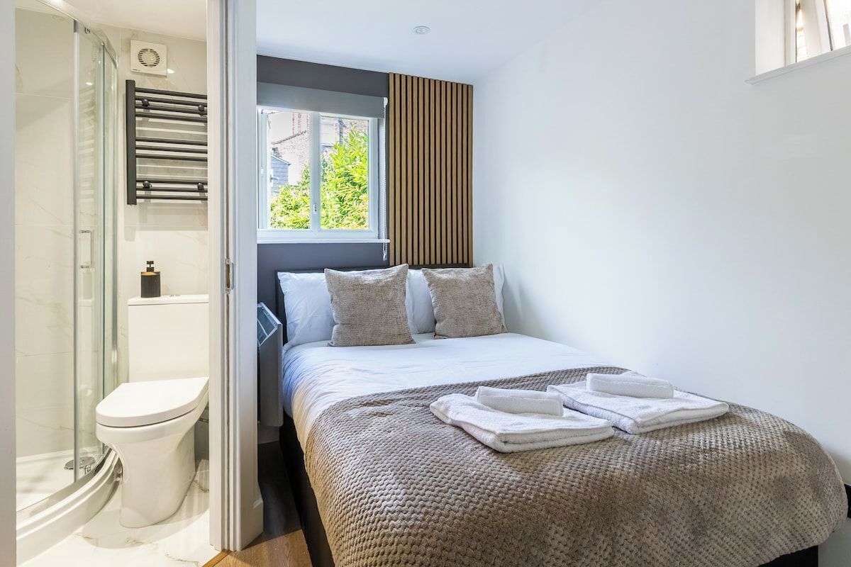 A bedroom with a bed, a window, a towel on the bed, and a shower area.