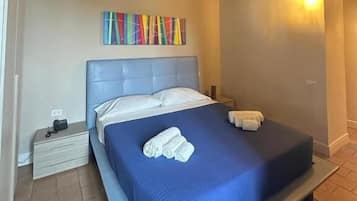 Een slaapkamer met een houten plafond, een bed met een blauwe spreideken, een kleurrijk kunstwerk aan de muur en een nachtkastje met een lamp.