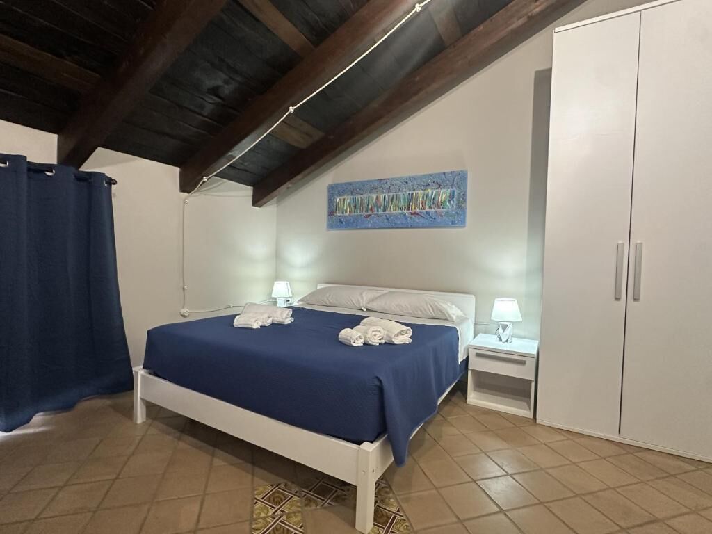 Un dormitorio con una cama, dos mesitas de noche, un armario y un techo con vigas a la vista.