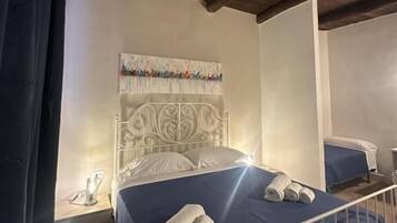Une chambre à coucher avec un lit en métal, une tête de lit ornée d’un panneau décoratif, une couvre-lit bleue et des serviettes enroulées posées sur le lit.