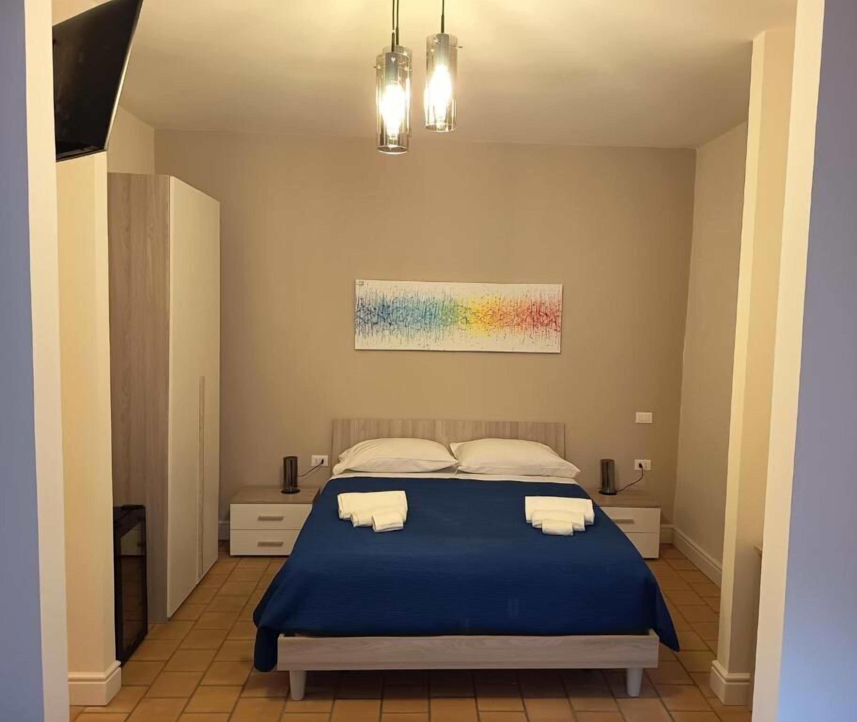 Ein Schlafzimmer mit Bett, Nachttischen, Wandbild und Deckenleuchte.