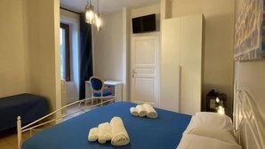 Una habitación de hotel con cama, escritorio, silla, armario y una lámpara en el techo.
