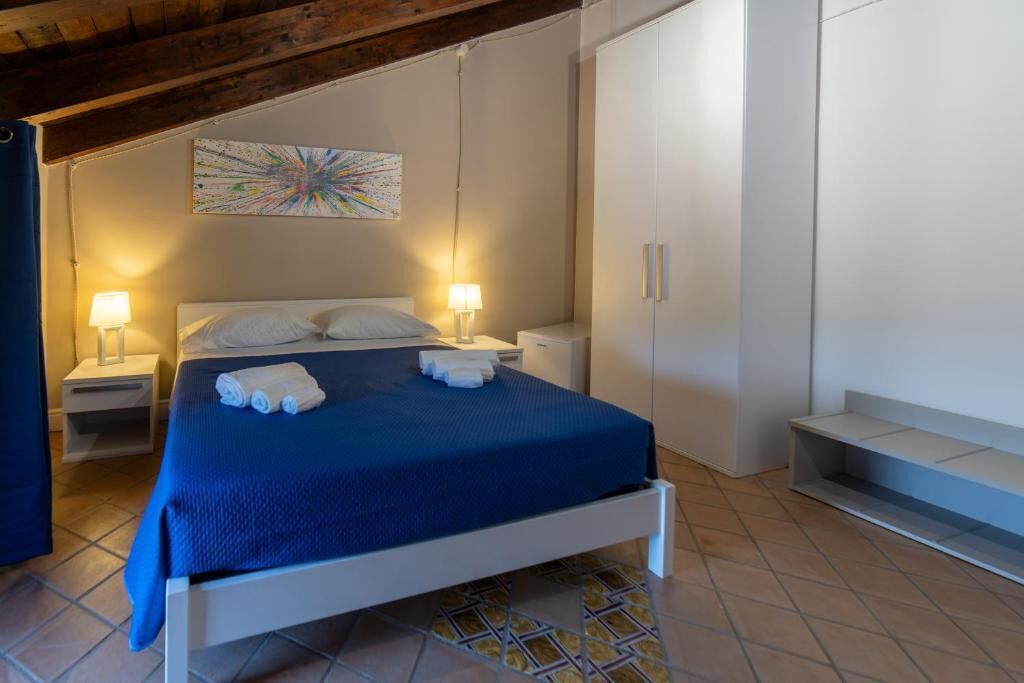 A bedroom with a bed, two bedside tables with lamps, a wardrobe, and a colorful abstract painting on the wall.