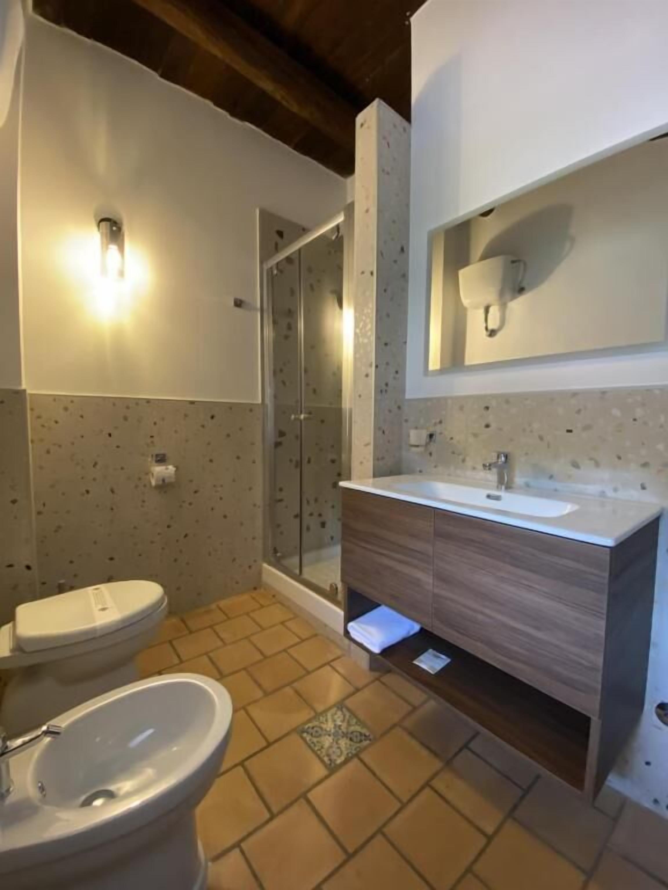 Une salle de bain équipée d’une douche, de toilettes et d’un lavabo, avec un carrelage au sol et un meuble-lavabo en bois.