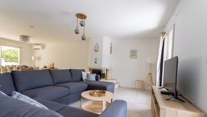 Ein modernes Wohnzimmer mit einer Eckcouch, einem kleinen runden Tisch, einem Fernseher auf einem Holzgestell und einem Kamin.