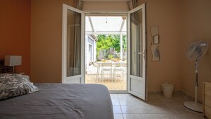 Ein Schlafzimmer mit einem Bett, einem Ventilator und einer geöffneten Tür zu einer Terrasse mit Tisch und Stühlen.