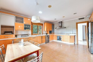 A modern kitchen with orange cabinets, a wooden dining table, and a stainless steel refrigerator. - LXR Villa Mirador del Sur, 5 Bedrooms, Ocean Views (Marbella)