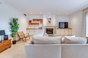 A modern living room with a sofa, a television, a fireplace, and a dining area with wooden cabinets. - LXR Villa Mirador del Sur, 5 Bedrooms, Ocean Views (Marbella)