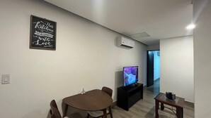 A modern living room with a dining table, chairs, a flat-screen TV, a small table, and an air conditioning unit. - Patriota Loft for 2, with amenities and parking (Monterrey)